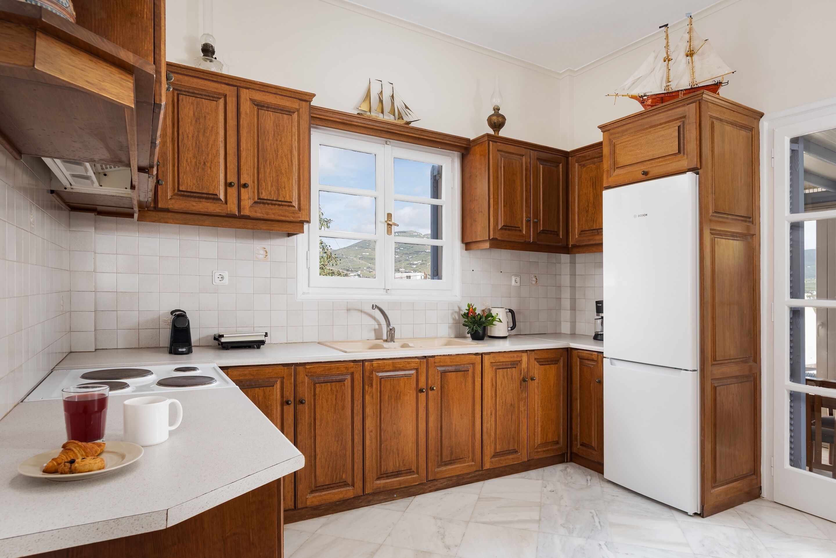 A kitchen with wooden cabinets, a white refrigerator, a sink, and a window with a view of the outdoors.