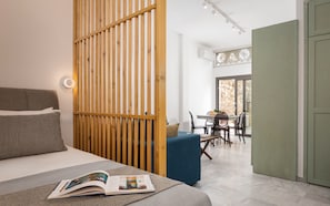 A modern bedroom with a bed, a wooden partition, a dining area with a table and chairs, and a view of the outdoors.
