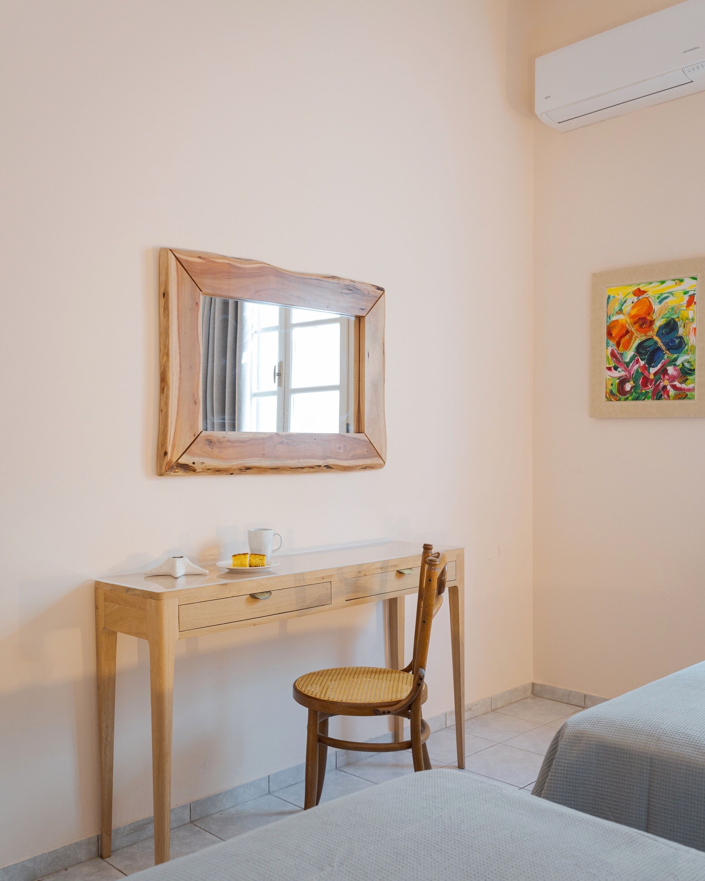 Um quarto com escrivaninha de madeira, uma cadeira, um espelho, um quadro e uma cama.