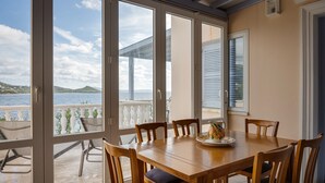 Un espace repas comprenant une grande table et des chaises, une vue sur la mer et les montagnes, ainsi qu’un balcon doté d’une balustrade.