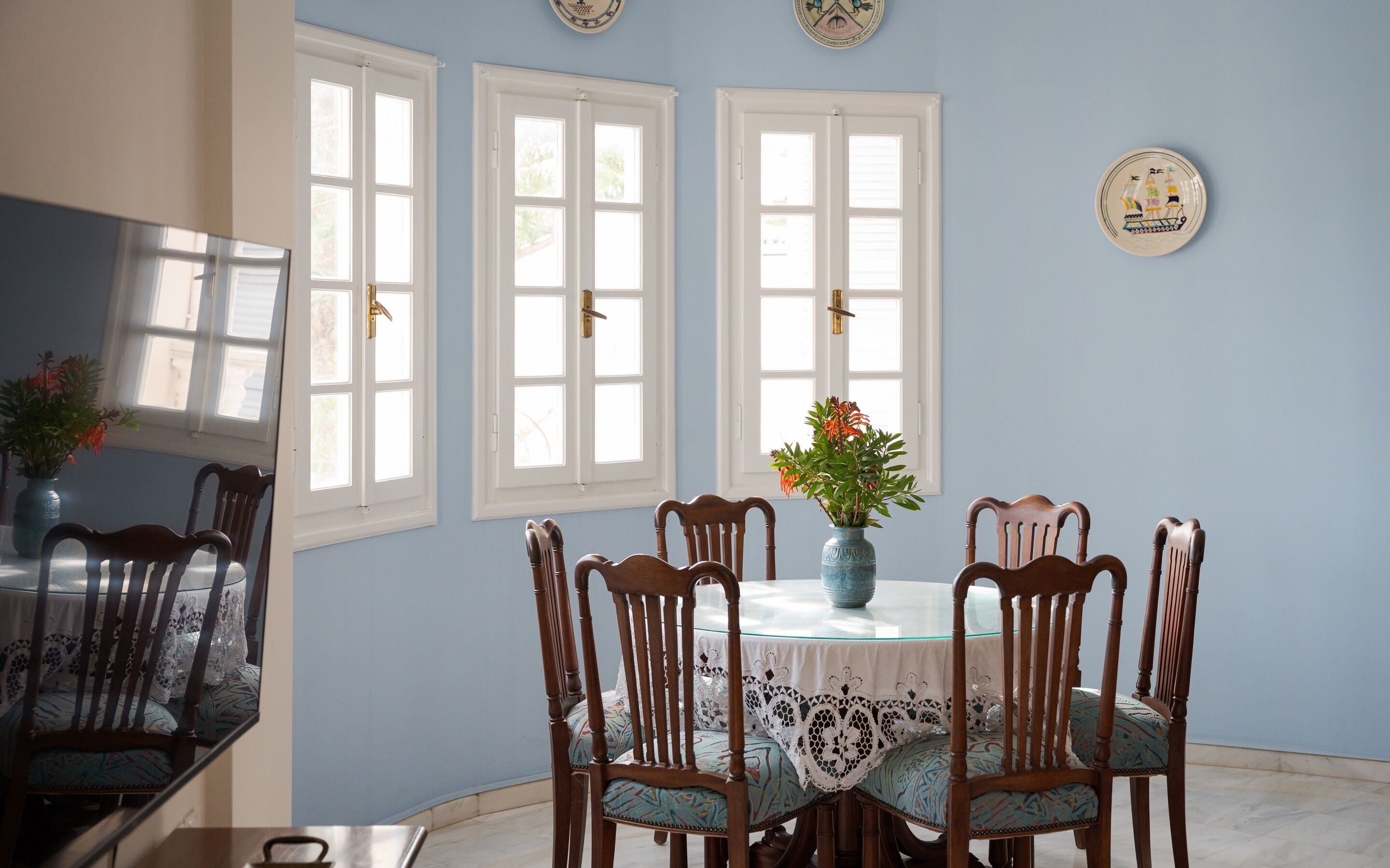 Un comedor con una mesa redonda, seis sillas de madera y un florero con flores.