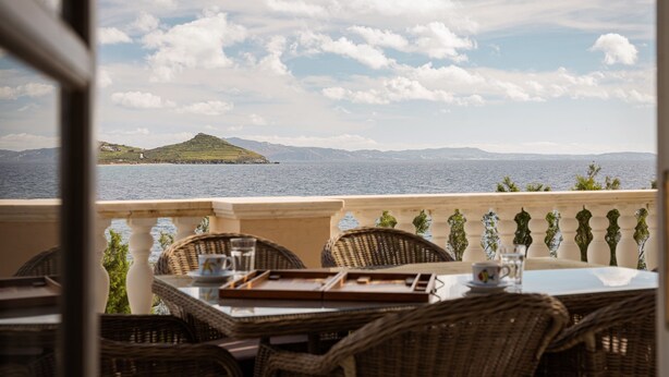 Une terrasse dotée de meubles en osier et d’une table dressée pour le repas, offrant une vue sur une étendue d’eau et sur la terre ferme au loin.