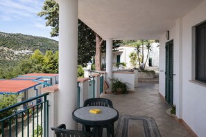 En balkon med et bord og stole, udsigt over det omkringliggende landskab, og en bygning med rødt tag.