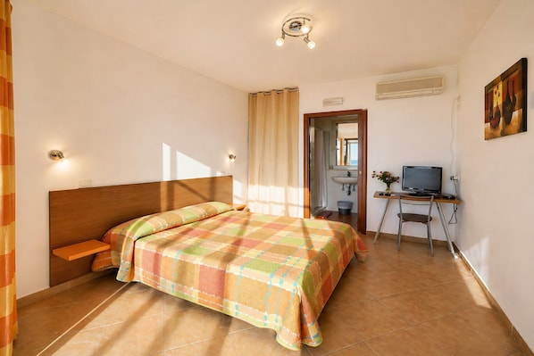 A bedroom with a bed, a desk, a chair, a television, and a bathroom visible through an open door. - San Michele - 3 - Bed & Breakfast with Sea View, Wi-Fi and Air Conditioning (Mattinata)