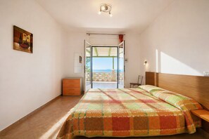 A bedroom with a bed, a nightstand, a dresser, a painting, and a balcony with a view. - San Michele - 3 - Bed & Breakfast with Sea View, Wi-Fi and Air Conditioning (Mattinata)