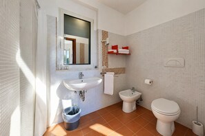 Un baño con lavamanos, bidé, inodoro y una ventana con cortina.