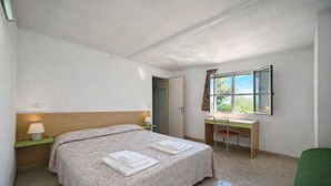 Quarto de hotel com cama, escrivaninha, cadeira e janela.