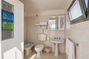Een badkamer met toilet, bidet, wastafel en spiegel.