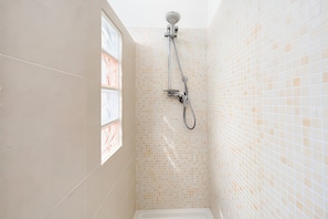Un baño con ducha, paredes de azulejos y una ventana.