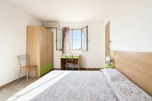 Un dormitorio con cama, escritorio, silla, armario y ventana.