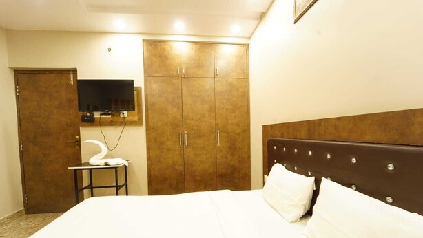 Ein Hotelzimmer mit Bett, Schrank, Fernseher und einem kleinen Tisch mit einem Handtuch.
