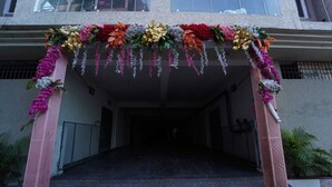 Ein Eingangsbereich mit einem blumengeschmückten Bogen, einem verschlossenen Weg und einer Gebäudefassade im Hintergrund.