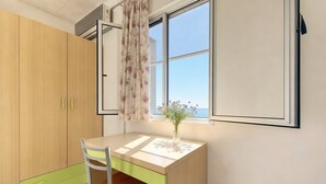 Ein Zimmer mit Schreibtisch aus Holz, einem Sessel, einem Fenster mit Aussicht und einem Vorhang.