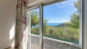 Ein Zimmer mit großem Fenster, Blick auf eine Küstenlandschaft und einem grünen Geländer.