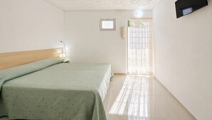 Ein Schlafzimmer mit einem Bett, einem Fenster, einem an der Wand montierten Fernseher und einer Tür mit Vorhang.