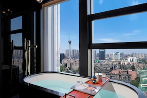A modern bathroom with a large window, a bathtub, and a view of a cityscape including a tower.
