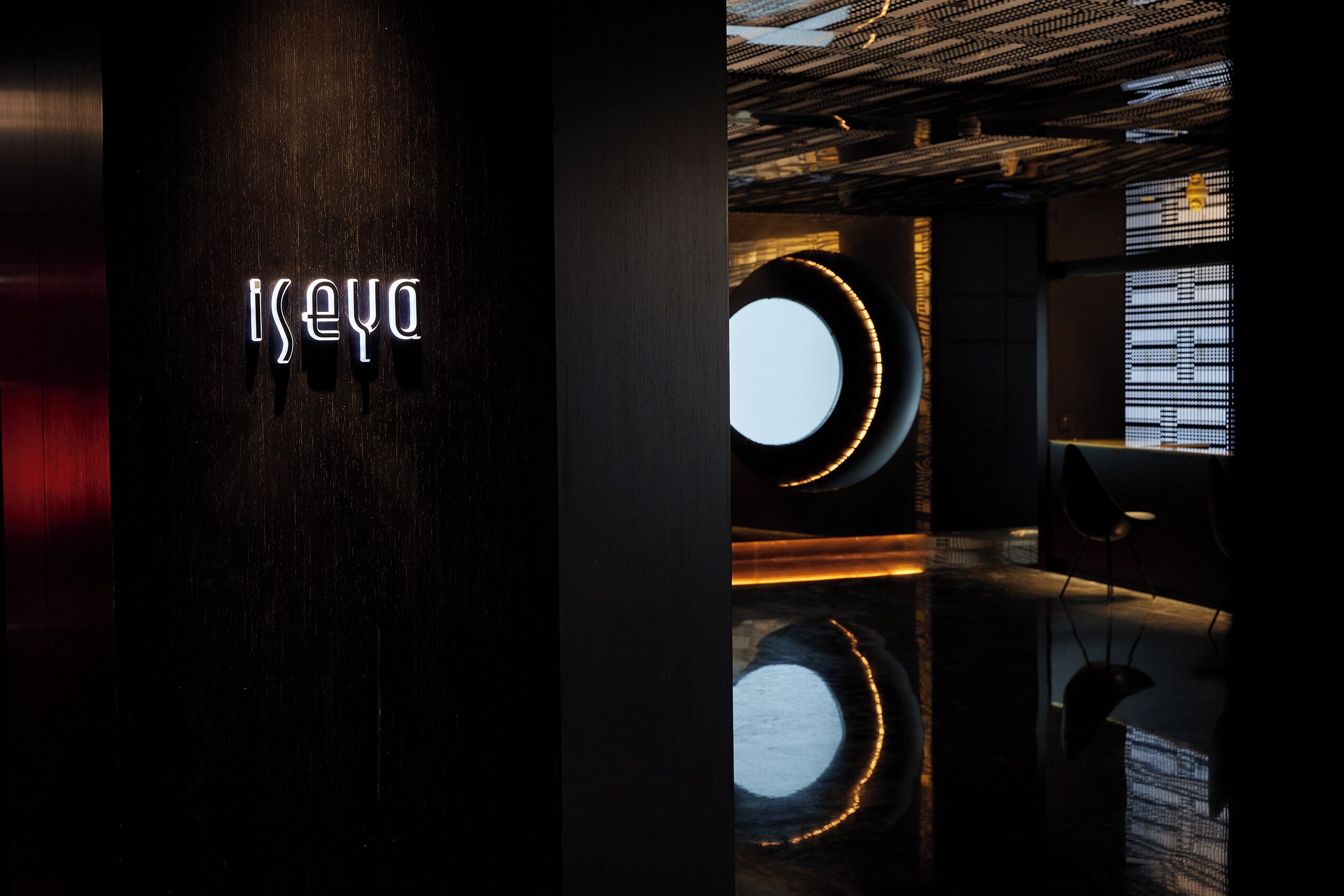 A modern interior with a neon sign reading "Iseya" and circular windows with illuminated edges.