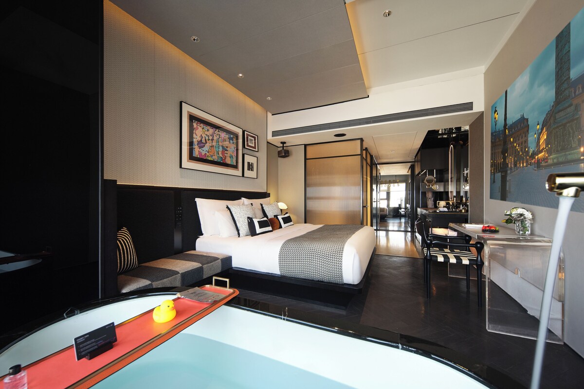 Une chambre d’hôtel moderne, dotée d’un grand lit, d’un bureau et offrant une vue sur le paysage urbain.