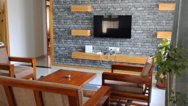 A living room with a stone wall, wooden furniture, a flat-screen TV, and a ceiling fan. - 2 BHK apartment in Hosapete for a relaxing stay (Hosapete)