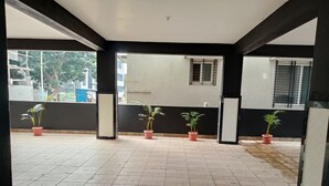 A covered outdoor area with tiled flooring, potted plants, and a view of buildings in the background. - 2 BHK apartment in Hosapete for a relaxing stay (Hosapete)
