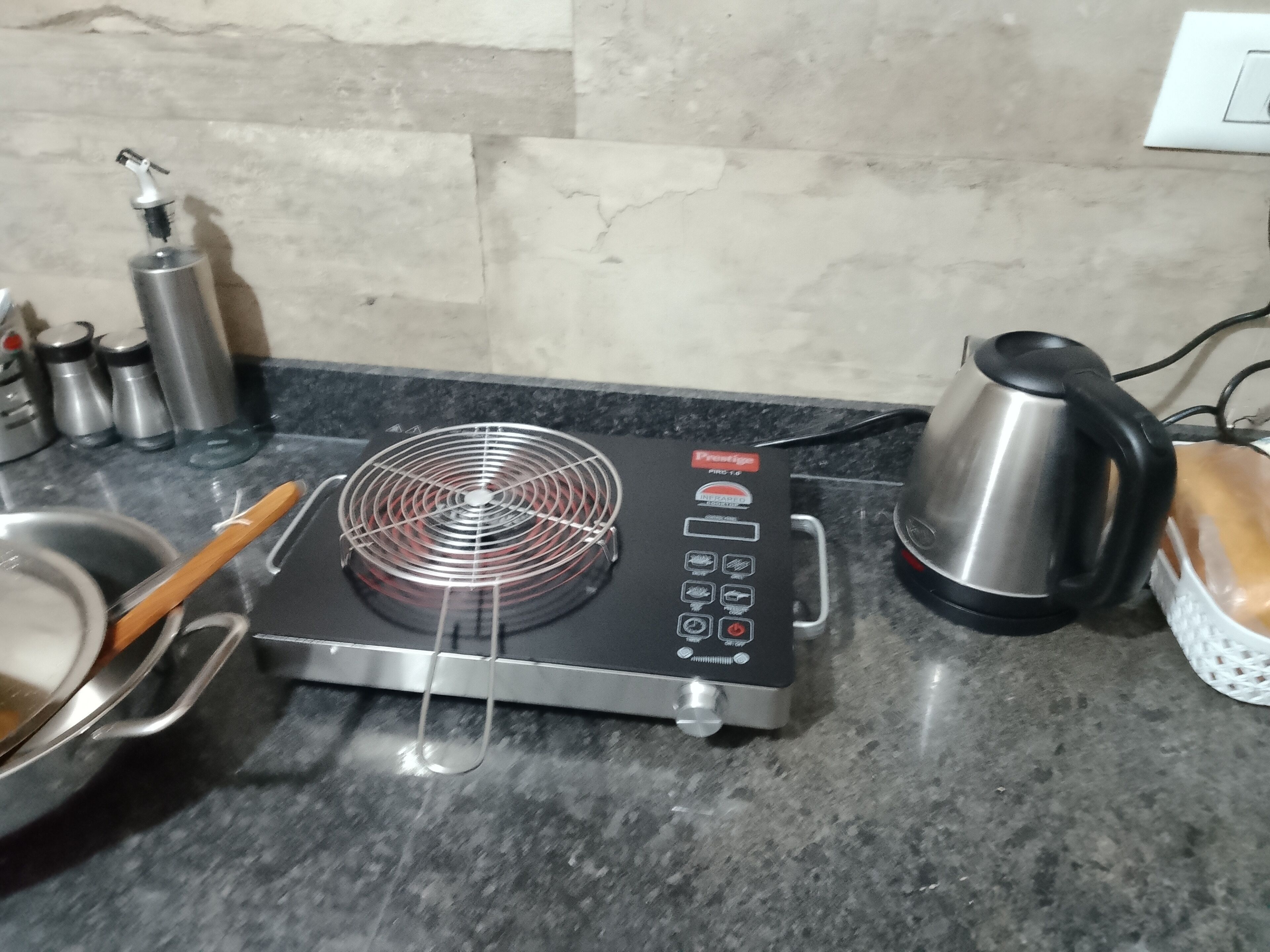 Une cuisine équipée d’une plaque de cuisson électrique mobile, d’une bouilloire et de récipients en acier inoxydable.