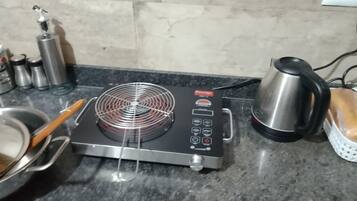 Une cuisine équipée d’une plaque de cuisson électrique mobile, d’une bouilloire et de récipients en acier inoxydable.