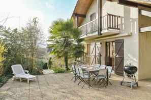 An outdoor patio with a table, chairs, a grill, and a lounge chair.