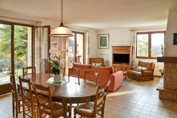 A dining area with a round table and chairs, a sofa, a television, and a fireplace.