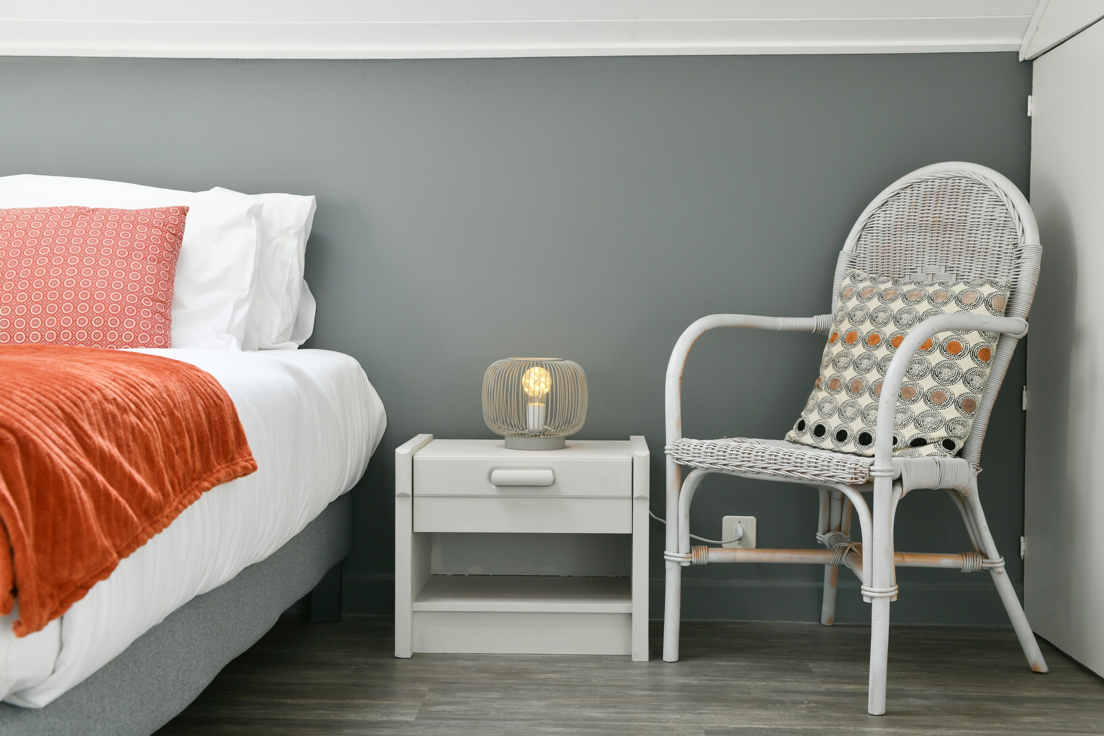 A bedroom with a bed, nightstand, chair, and bedside lamp.