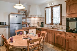 A kitchen with wooden cabinets, a refrigerator, a stove, and a dining table with chairs.