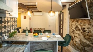 Un espace repas avec une table en marbre, des chaises vertes, des suspensions et un mur en pierre.