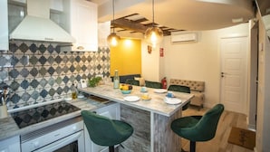 Une cuisine avec un îlot central, une cuisinière et un évier. On y trouve deux chaises vertes et un canapé beige.