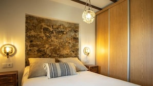Une chambre à coucher avec une tête de lit en pierre, deux lampes de chevet, un lit avec une literie blanche et un luminaire suspendu.