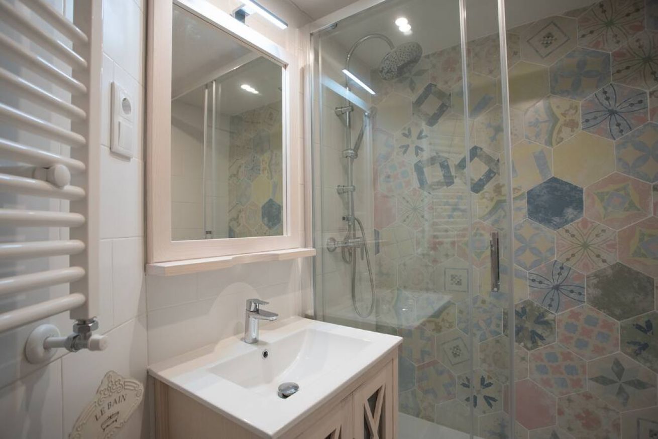 Een badkamer met een douche met glazen wand, een wit wastafeltje en een spiegel erboven.