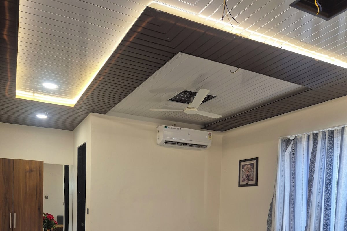 A bedroom with a bed, a wooden wardrobe, an air conditioning unit, a ceiling fan, and a window with curtains.