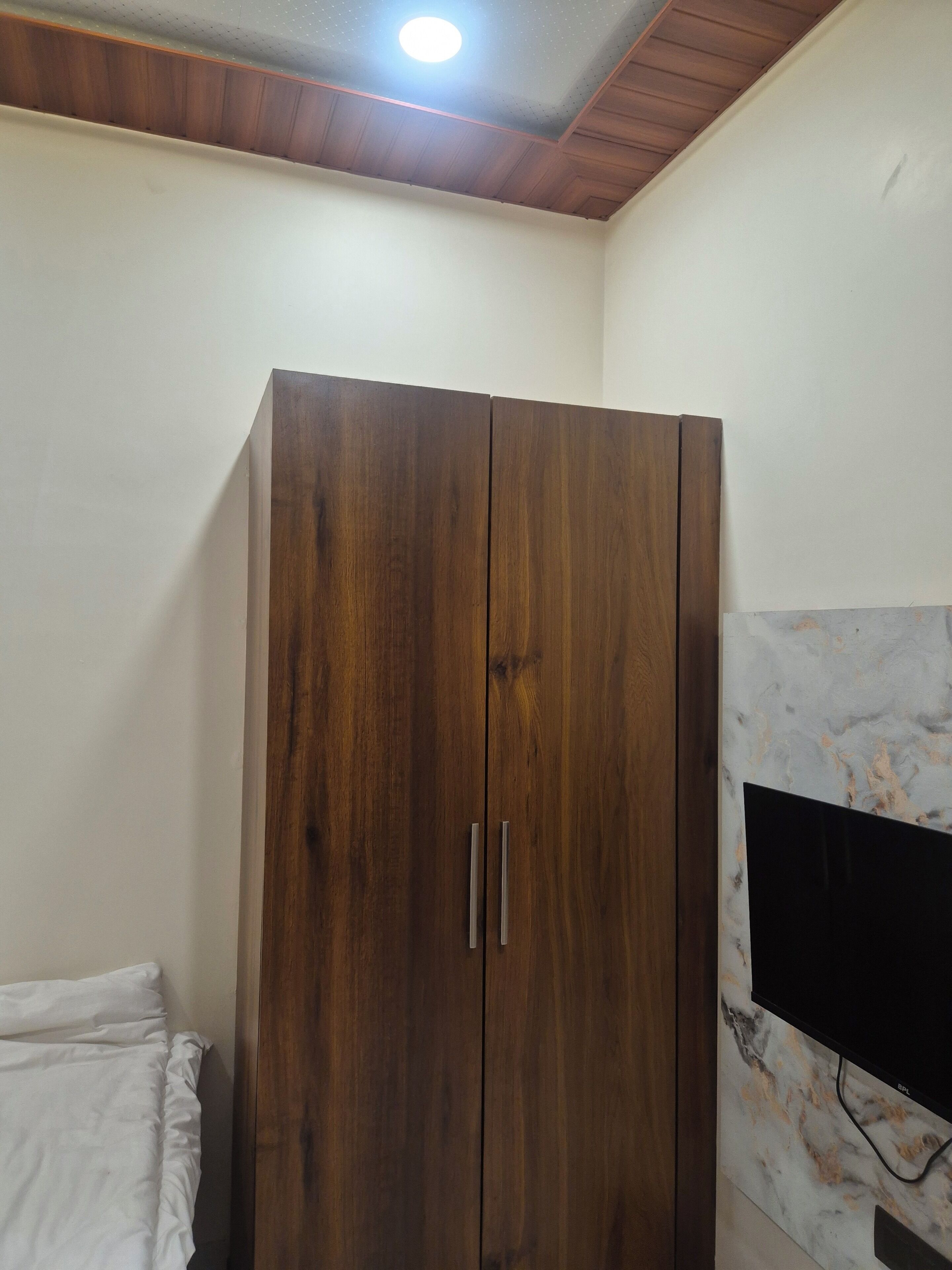 Una habitación con un armario de madera, una cama y un televisor instalado en una pared de mármol.