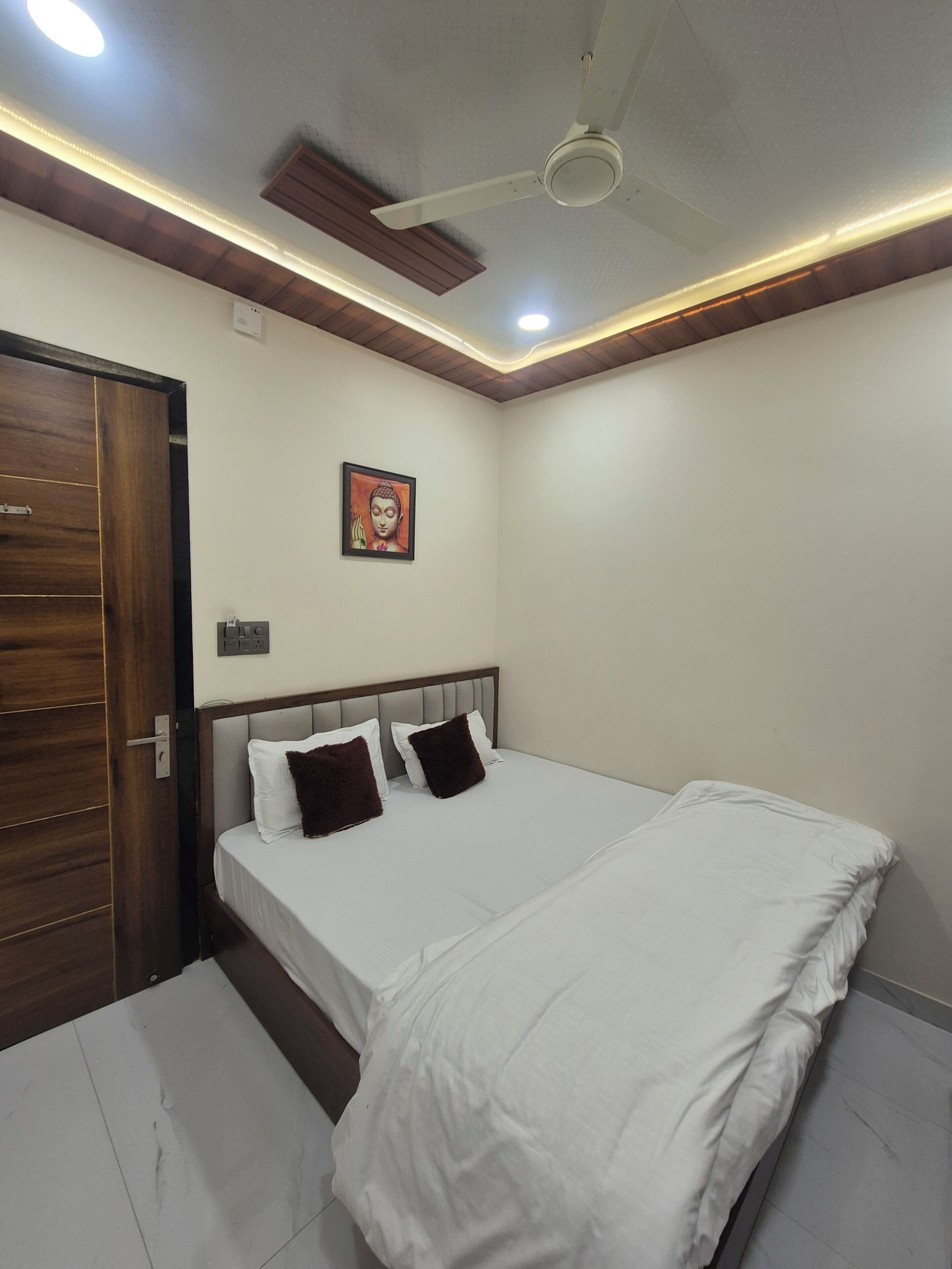 Un dormitorio con una cama, un ventilador de techo, una lámpara fijada a la pared y una puerta de madera.