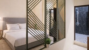 A modern bedroom with a bed, a potted plant, and a large mirror reflecting the room.