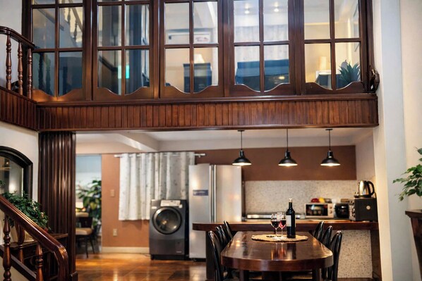 A modern kitchen with a dining area, wooden staircase, and large windows.