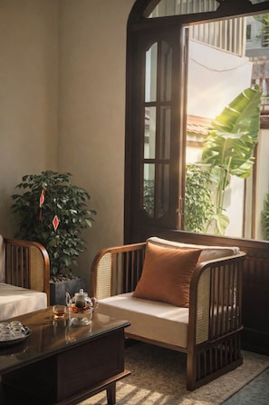 A cozy seating area with a cushioned sofa and a wooden table, a large window with a view of greenery, and a potted plant.
