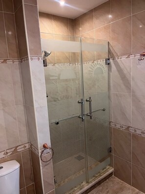 Un baño moderno con mampara de vidrio, azulejos color beige y un inodoro.