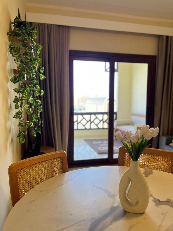 Un comedor con una mesa redonda, sillas, un jarrón con flores y vistas al exterior por un ventanal.