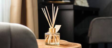 Una mesita de madera con una botella de vidrio y difusor de cañas en una habitación moderna con un sofá gris y una silla negra.