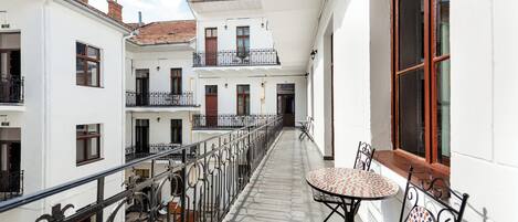 A covered balcony with a table and chairs, a railing, and a view of adjacent buildings.