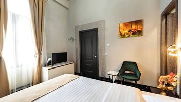 Habitación de hotel con cama, escritorio, computadora, silla y un cuadro en la pared.