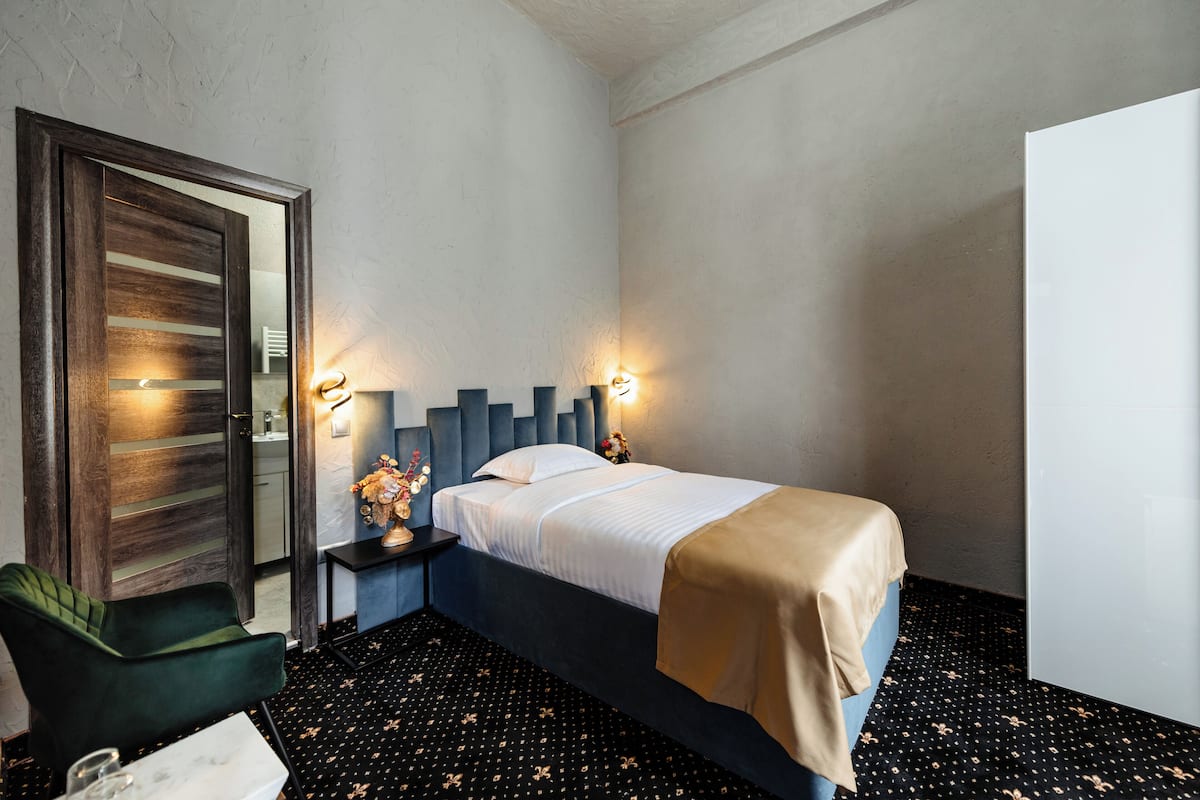 A hotel room with a bed, a chair, a nightstand, and a mirror.