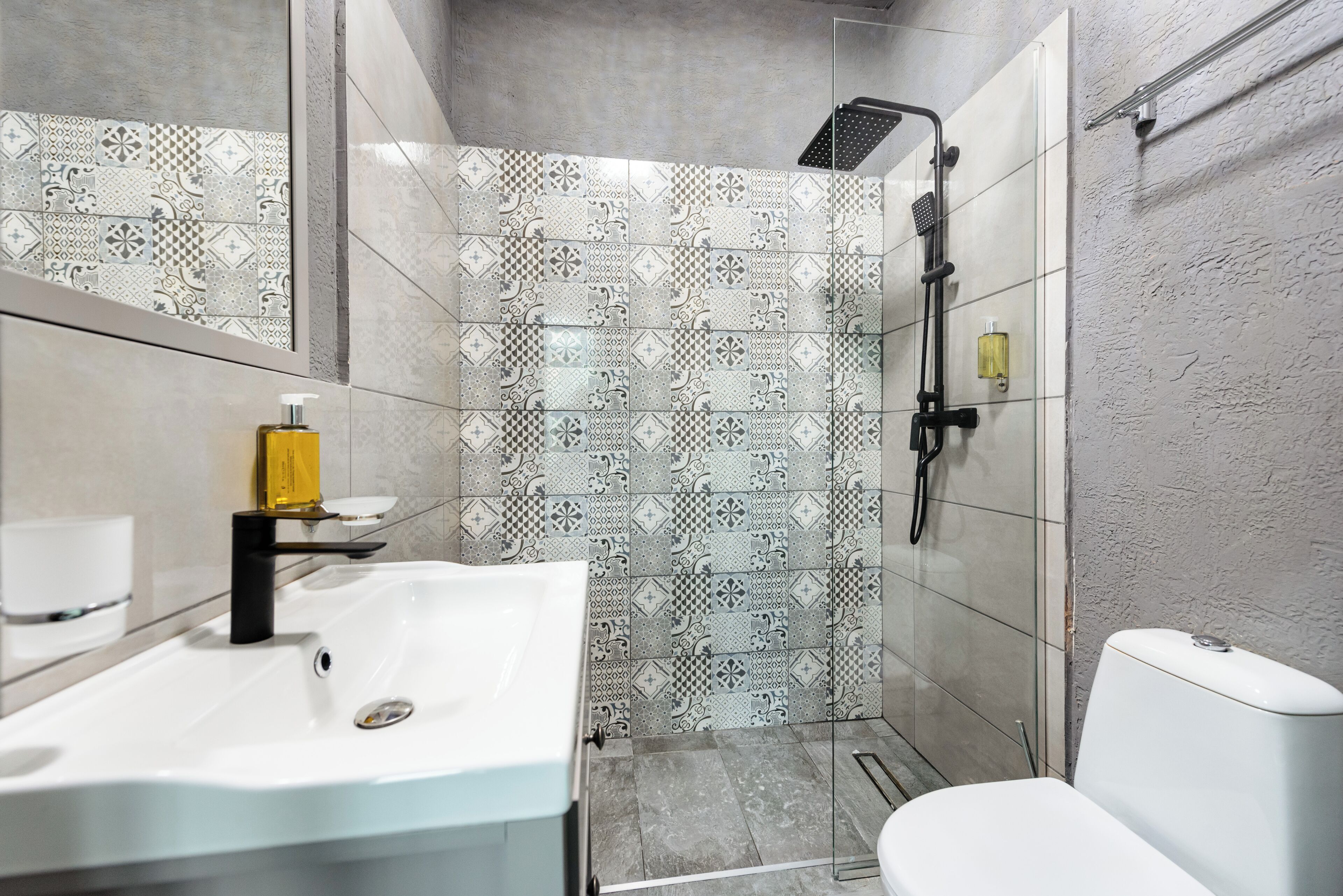 A modern bathroom with a white sink, a glass shower enclosure, and patterned tiles.