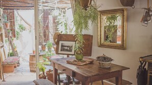 Une table en bois rustique, accompagnée d’un banc, entourée de plantes en pot et d’une bouilloire verte.