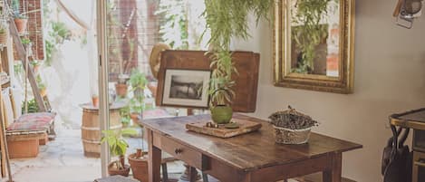 A rustic wooden table with a bench, surrounded by potted plants and a green kettle.