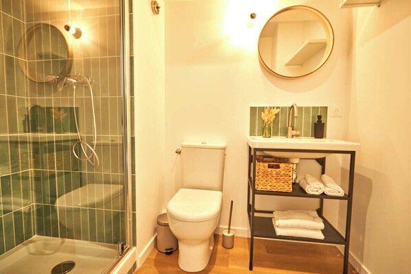 A bathroom with a glass-enclosed shower, a toilet, a sink with a mirror, and a shelf with towels. - La Quinta Bordeaux-Bègles (Bègles)